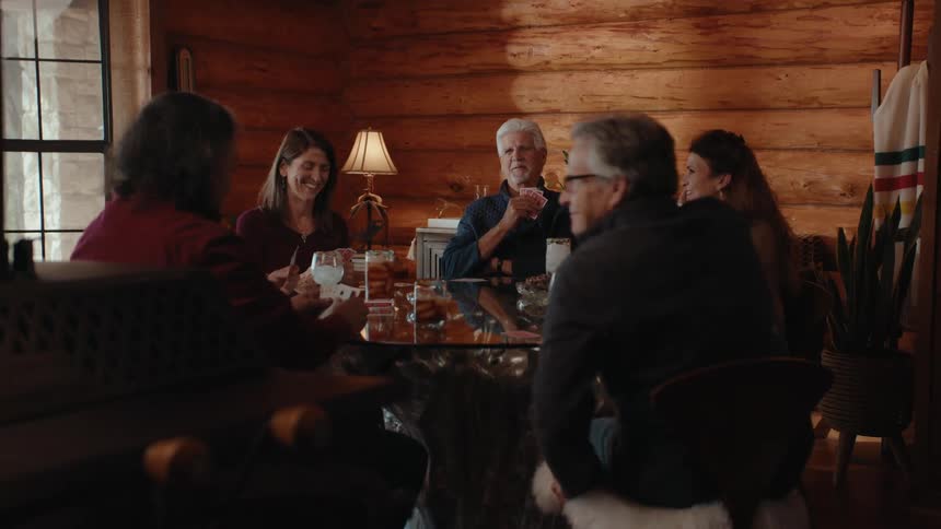 A group of friends sit around a table playing cards laughing and with drinks