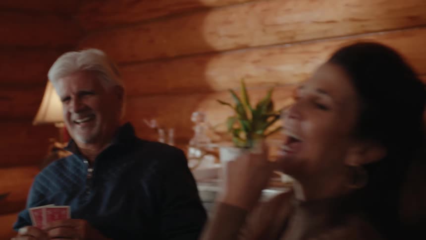 A man and a woman are laughing and playing cards at a table with the focus on their faces and hands