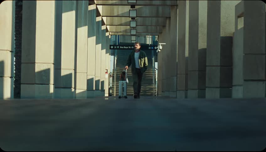 Traveler pulls along his rolling suitcase while walking away from an outdoor staircase outside a terminal