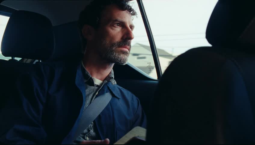 A man sitting on the backseat of a car holding and looking at a book or manual with diagrams