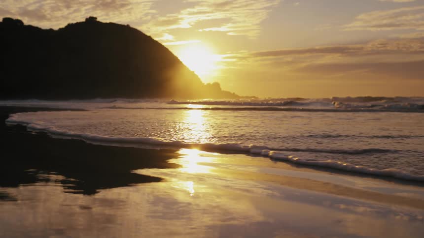 Beach landscape with waves hitting the sand and the sun on the horizon