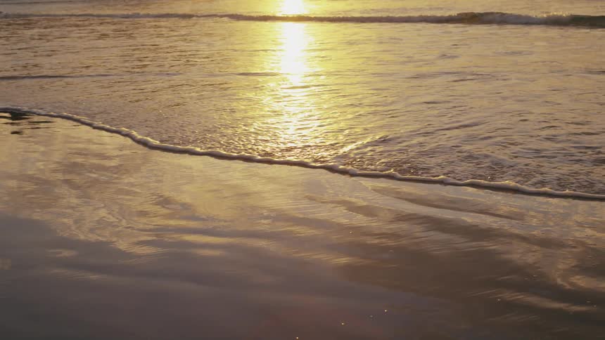 The sun sets over a sandy beach reflecting off the wet sand and gentle waves