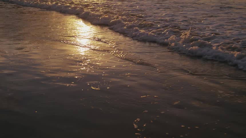 Tide extending over a beach reflecting the sun light outdoors during dusk or dawn