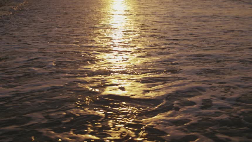 Ocean water meets wet beach sand with golden sun reflection