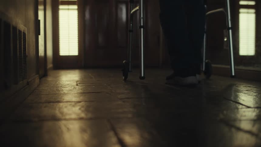 Legs of a person walking with a walker down a hallway