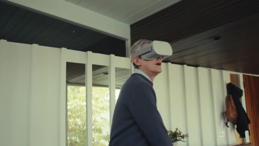 A person wearing a virtual reality headset is standing in a modern welllit room interacting with the virtual environment using hand gestures