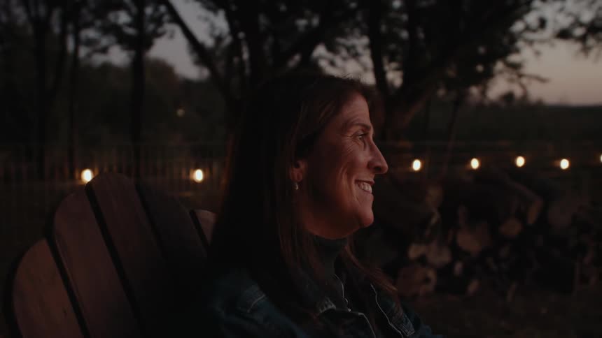 Woman sitting on a wooden chair in a natural environment at dusk and with a happy facial expression