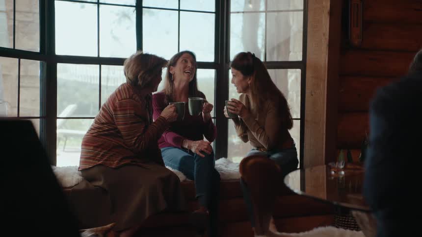 Three women of different ages sitting with mugs in their hands talking and laughing