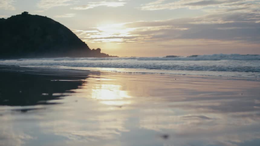 Landscape of a beach with the sea water reaching the sand and the sun on the horizon