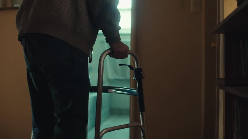Hands of an elderly person leaning on a walker and heading towards a room in the house