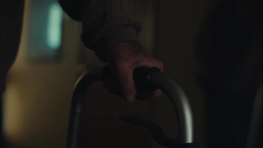 An elderly persons hand grips the handle of a walker