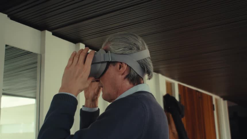 Mature man standing in front of a mirror setting up a vr headset on himself indoors during daytime