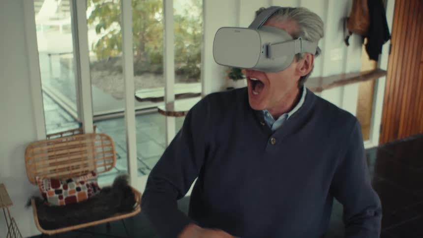 A man wearing a virtual reality headset raises his hand while playing