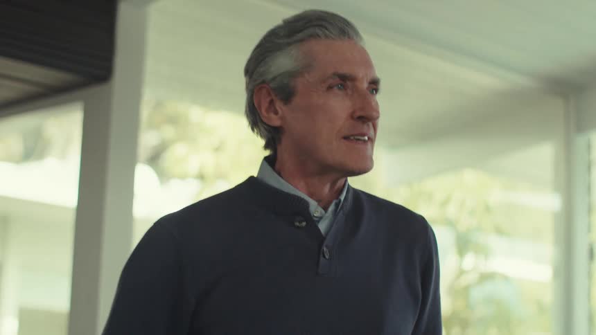 A grayhaired man holding a virtual reality headset and he is smiling and then starts looking in front of him