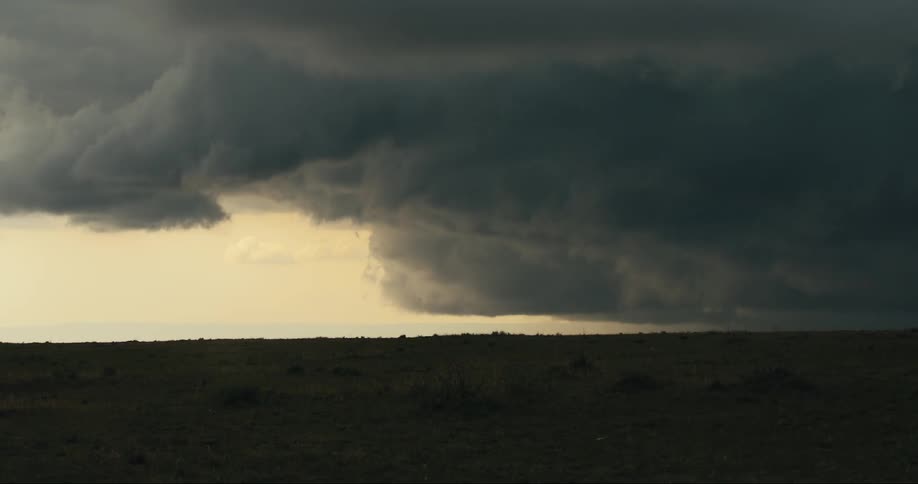 Heavy dark clouds on the horizon next to a plain field with vegetation outdoors