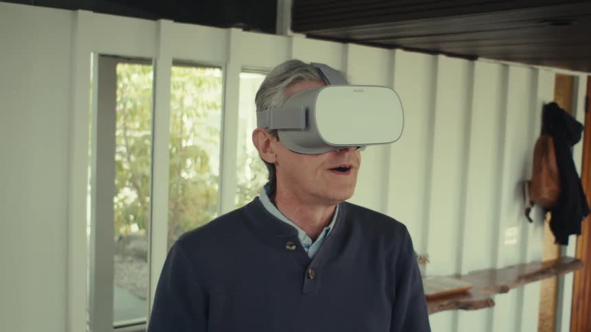 A gray haired man putting a vr glasses on his head and he gets excited and opens his mouth