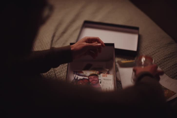 A person examining a sealed envelope a jar and some pictures among a collection of mementos