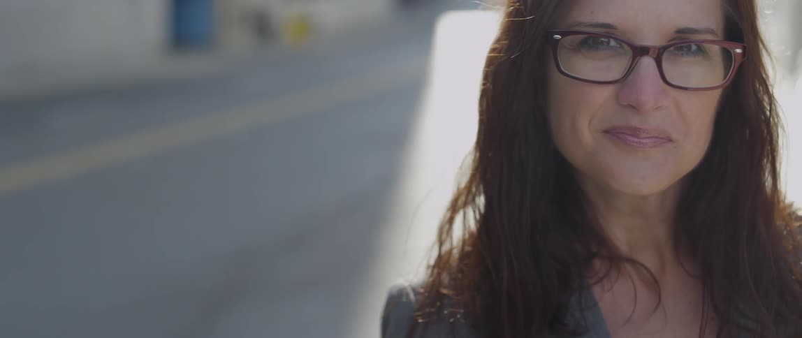 Woman wearing glasses smiles and tosses hair on a sunny day