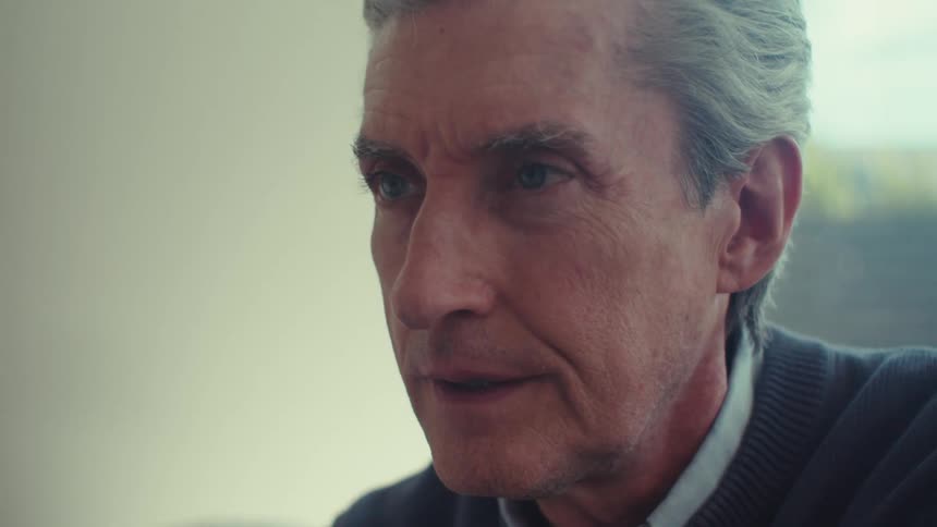 Gray haired sweater wearing man sits and thinks