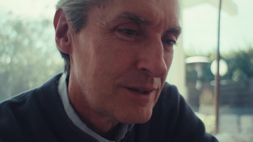 Older man smiles while sitting in his living room and viewing on a device