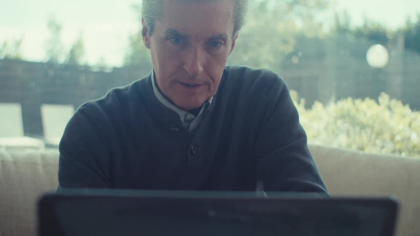 Man sitting on a couch looking at a laptop computer with anxiety indoors during day time