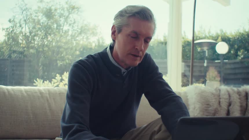 A clip of a man operating a laptop in the living room