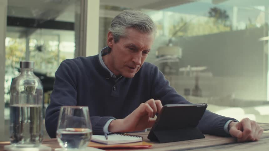 Man sitting at a table with a glass of water and interacting with a small tablet