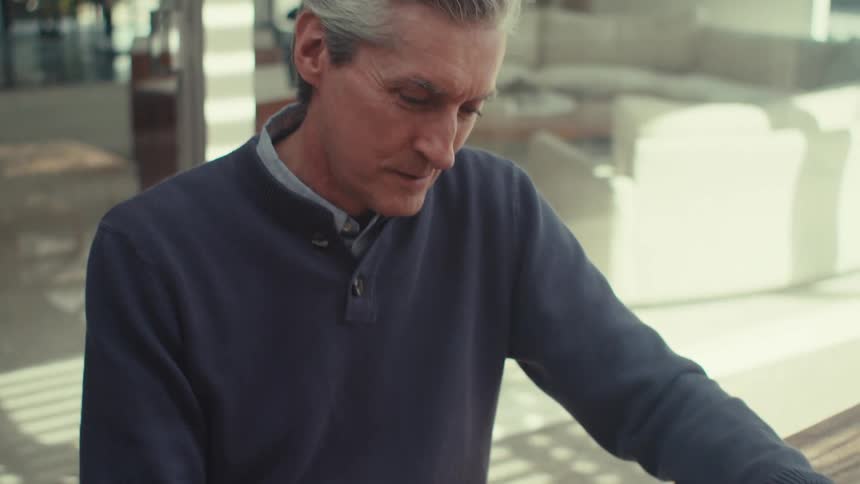 Man sitting at a table in an outdoor area of the house typing on a tablet