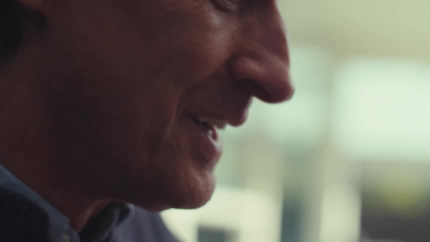 A face of a man who is talking to someone in front of him and he raises his hands and his thumbs up