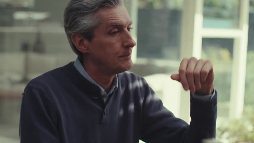 A middle aged man sits at a table engaging in a serious video call on a tablet