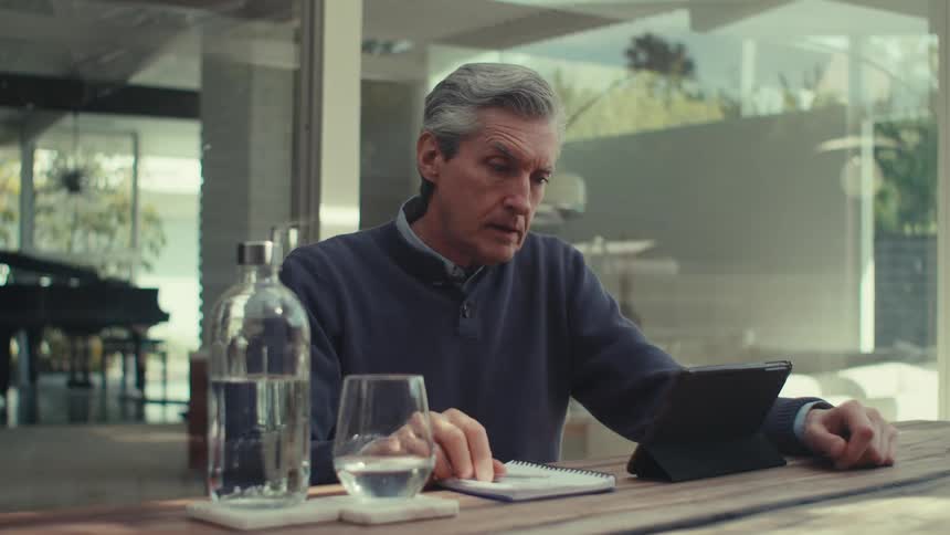 Older man upset by contents on tablet takes a sip of water