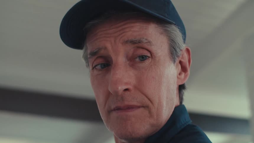 A man wearing a dark cap and a dark shirt is standing indoors