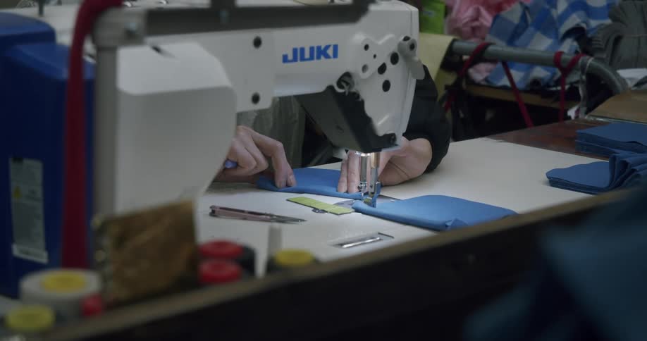 Close up of hands operating a sewing machine working with blue fabric