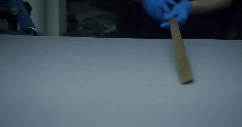 Gloved hands use a wooden ruler to measure a large piece of cloth