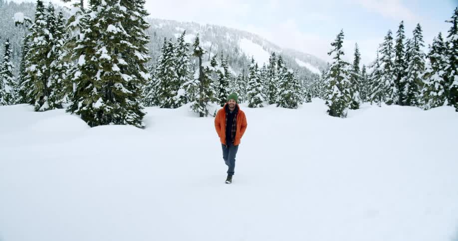 Smiling man walks across a snowy field near conifer trees on a winter day