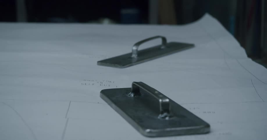 Gloved hands place square weights over a clothes pattern