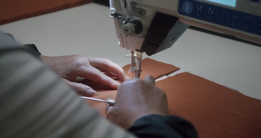 Close up of hands operating a sewing machine working with orange brown fabric