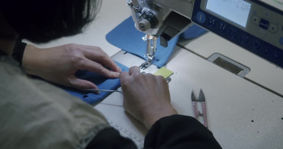 Woman uses a tool to maneuver a piece of fabric under the sewing machine presser foot