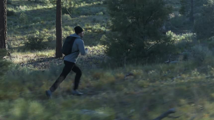 A man wearing a backpack runs up a trail in an evergreen forest