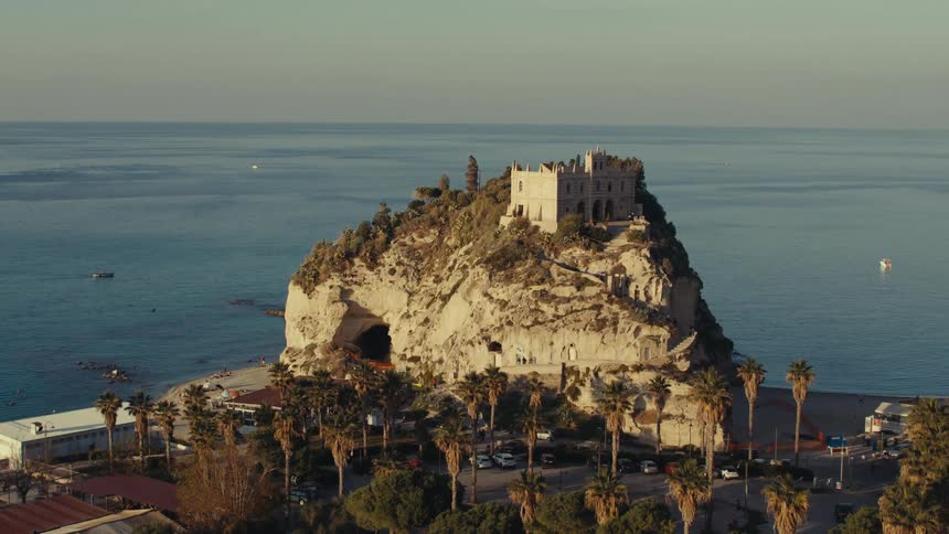 A white building on top of a large stone hill facing the sea