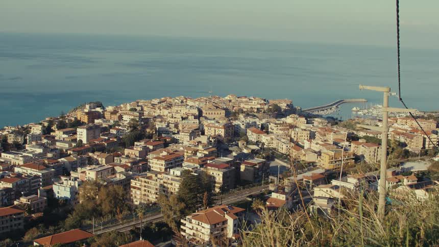 Highway passes through apartment buildings near a grass covered hill in a coastal town