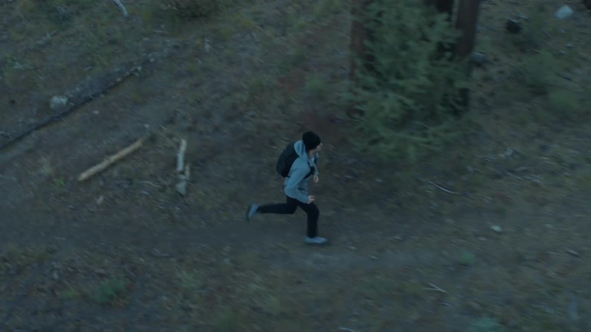 A man runs up a trail in an evergreen forest