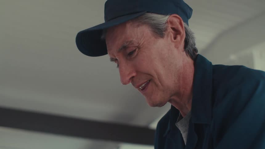 An older man wearing a blue cap and shirt meticulously working on a light switch