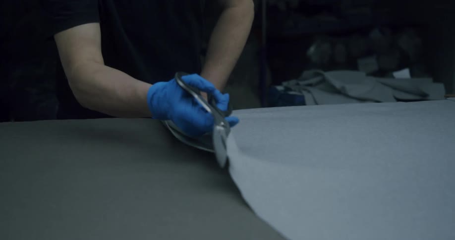 A tailor cuts a sheet of fabric with scissors