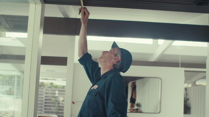 A man in a cap and workers clothes is measuring the ceiling using a tape measure