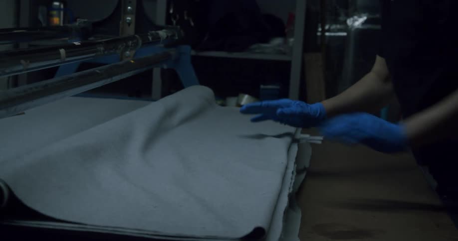 Hands with blue gloves handling a gray fabric