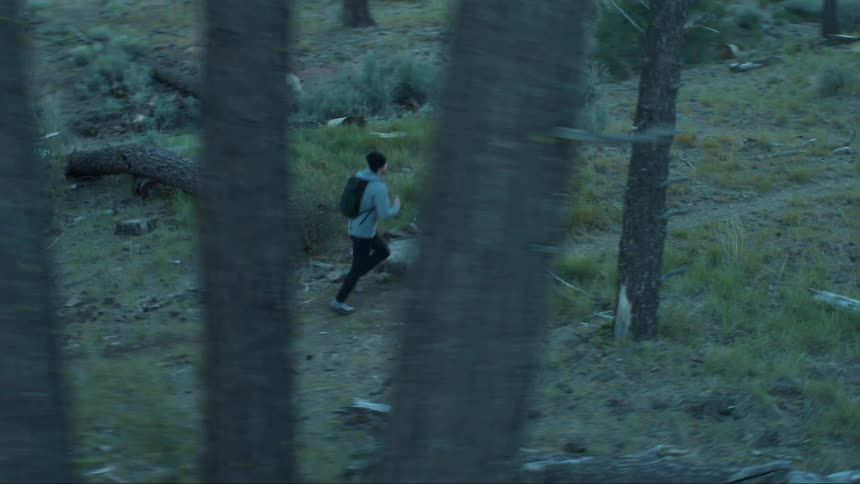 A person is running through a grassy wooded area with a backpack on