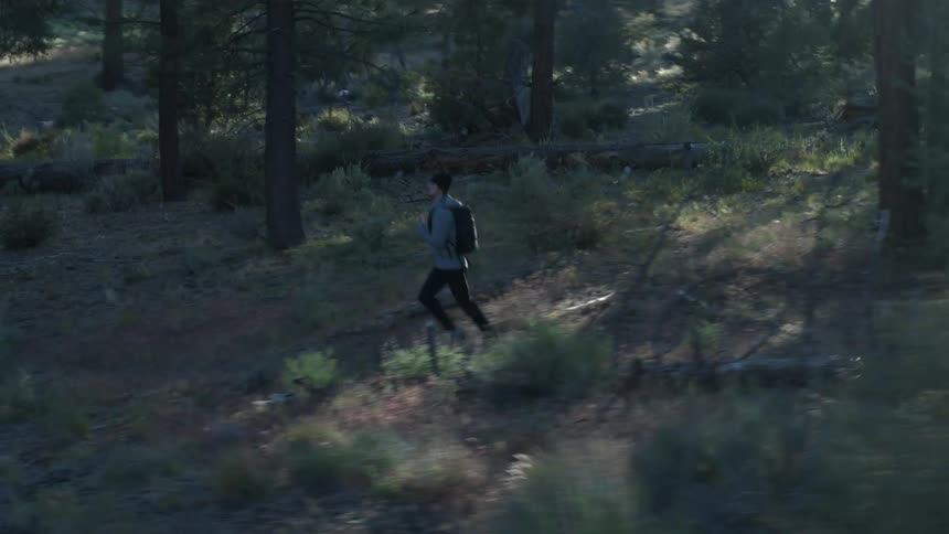 A man with a backpack and wearing a hat is running in a forest