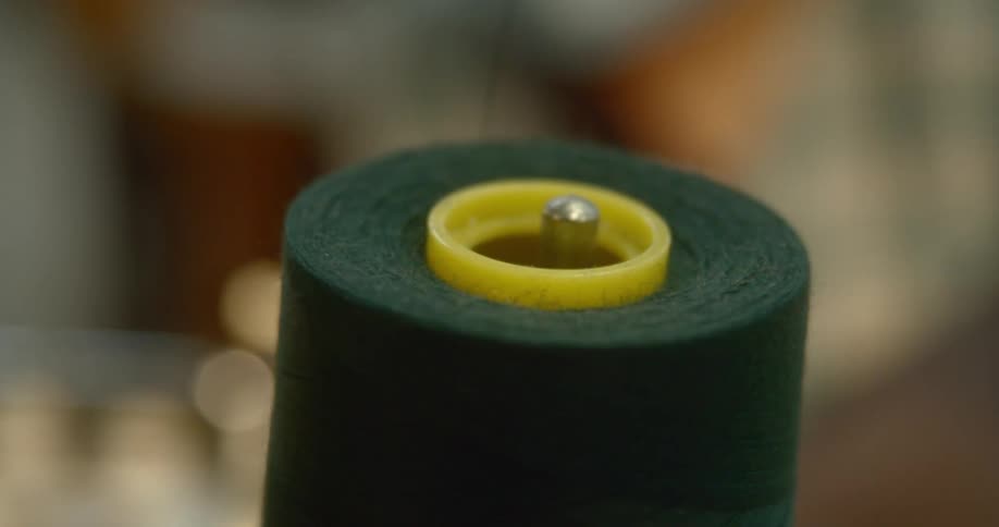 Sewing thread in a spool next to a person sewing indoors