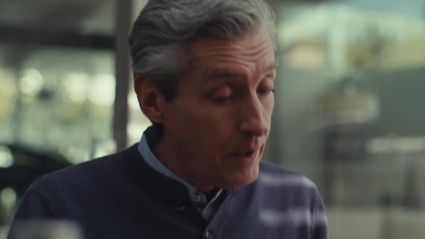A man with gray hair wearing a dark jacket is standing outdoors having a conversation
